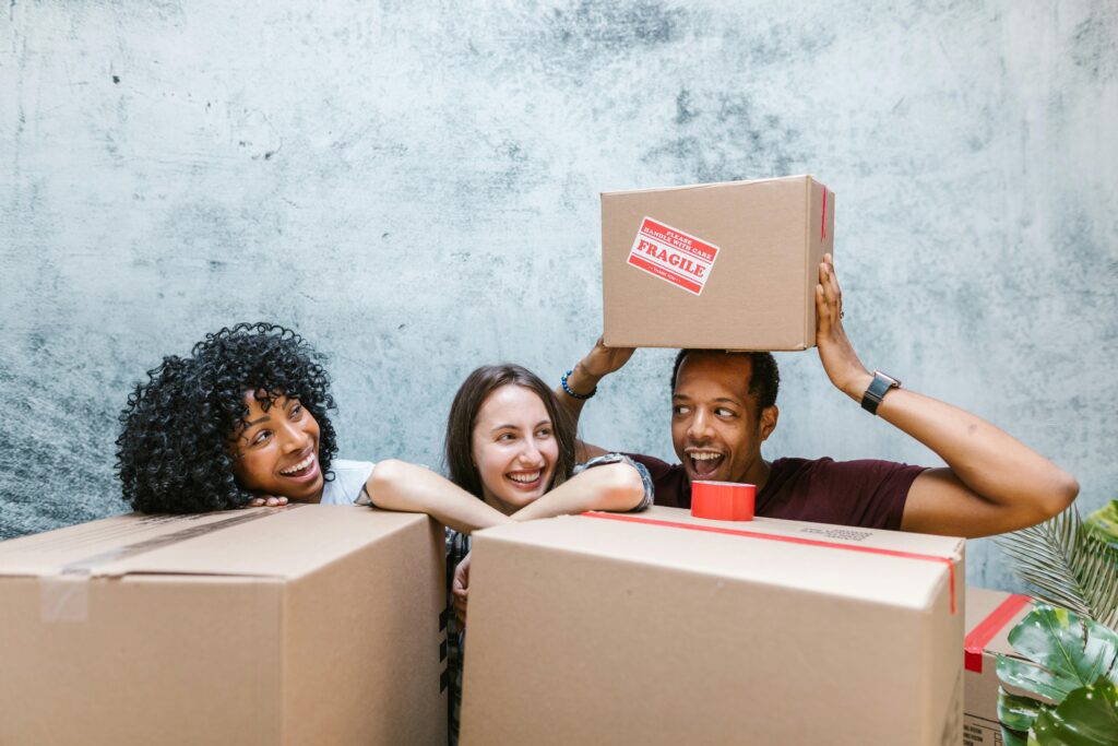 Diverse group of friends smiling while packing moving boxes. Relocation and new beginnings.