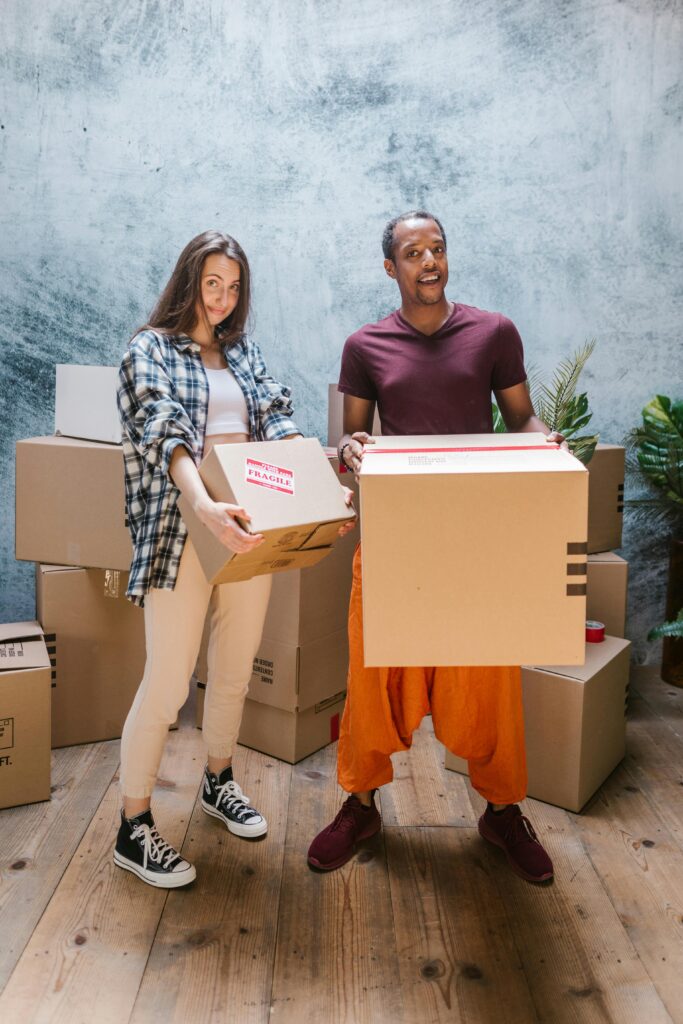 Two young adults smiling while moving boxes into a new home.